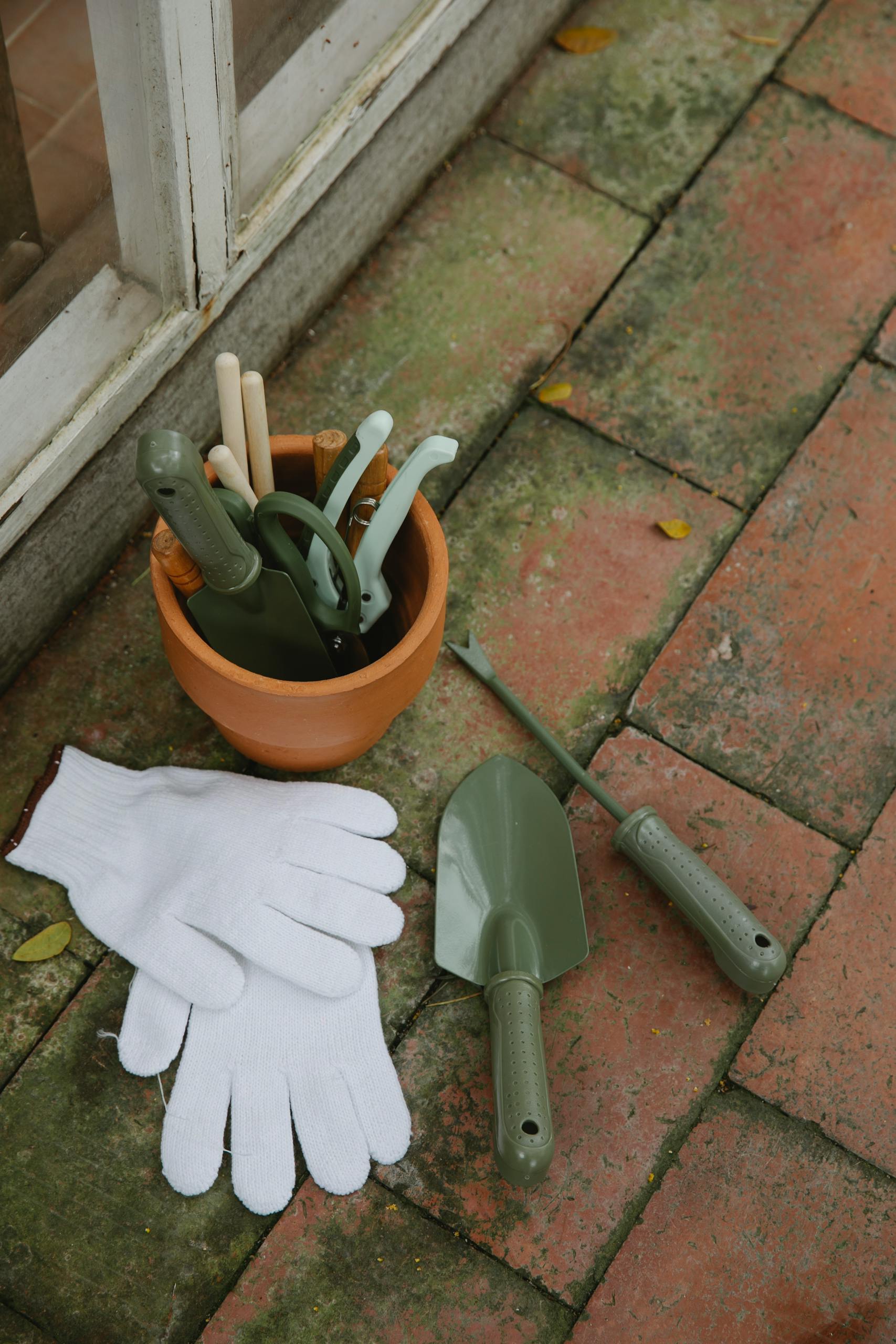 From above of various gardening instruments including shovel hoe pruner placed on tilled floor near pair of gloves